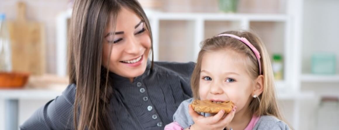 Smiling woman watching young girl eat a peanut butter sandwich