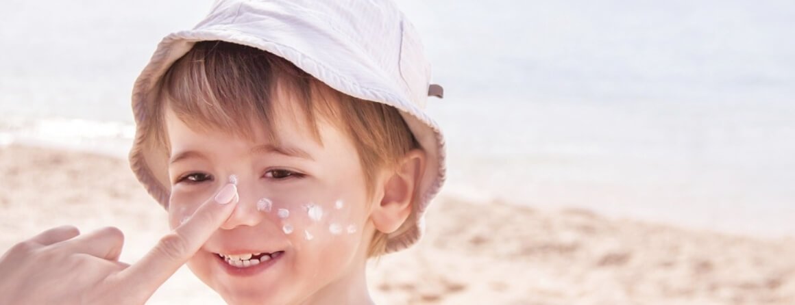 Smiling young boy at the beach having sunscreen applied to his face.