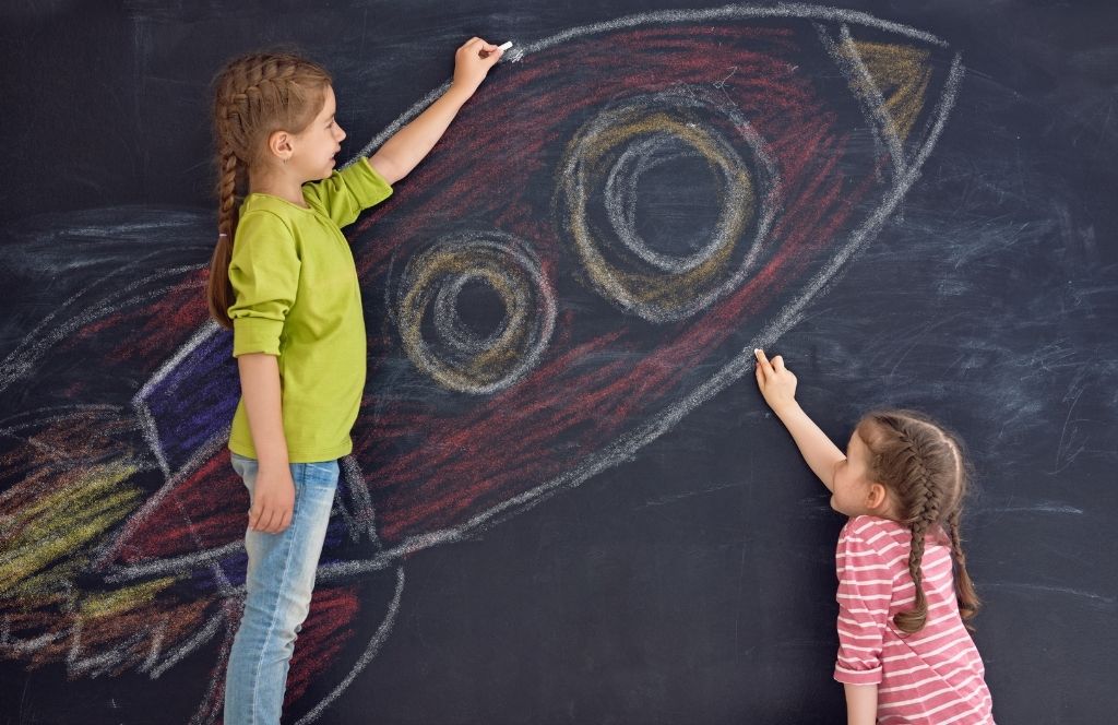 Girls drawing a rocket on a blackboard