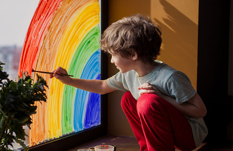 Child painting rainbow on a window
