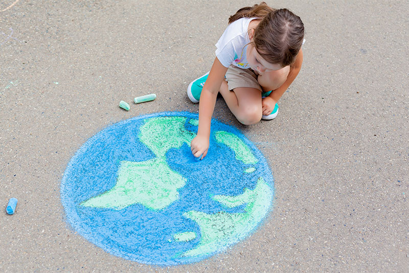 Girl drawing the world in chalk on the ground