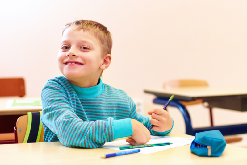 Happy child with a rare genetic disorder, sitting in a classroom