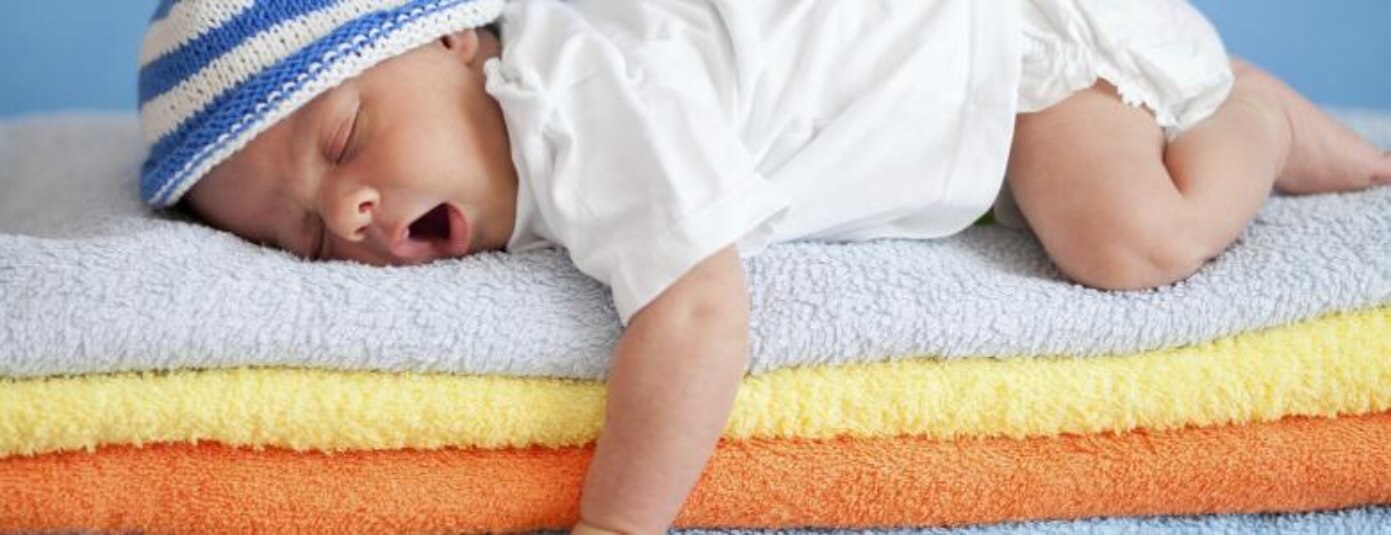 Yawning infant laying on stacked towels