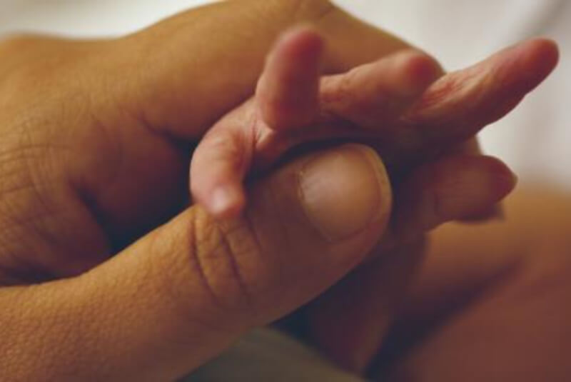 Womans hand holding the hand of a newborn infant