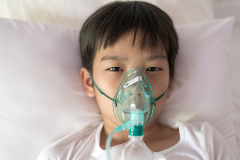 asian boy with face oxygen mask lay on a white bed at hospital