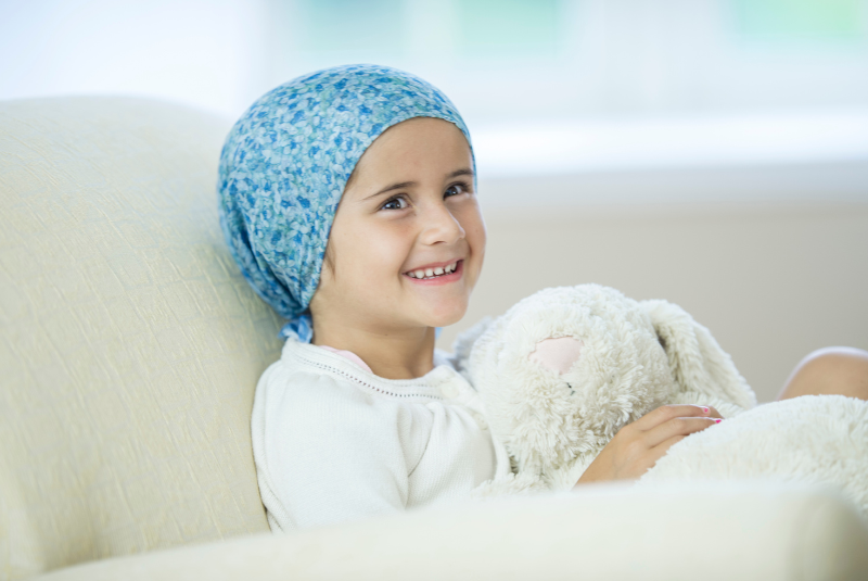 Smiling girl with cancer hugging a teddy bear