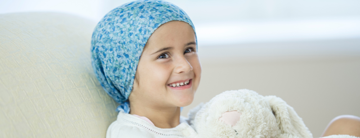 Smiling girl with cancer hugging a teddy bear