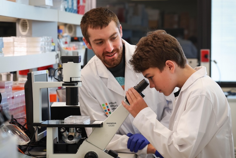 Cystic fibrosis patient Lewis with MCRI Dr Louis Perriman looking through a microscope. Image credit: David Caird, courtesy of News Corp