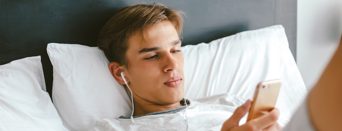An adolescent male in bed looking at social media on his phone
