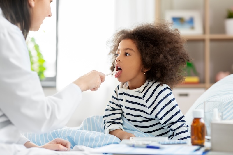 Child has their throat checked by doctor