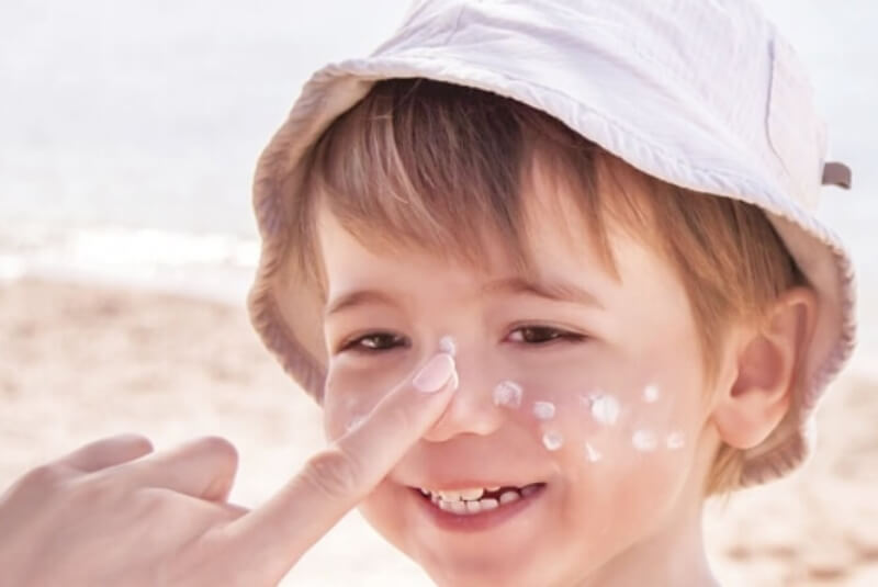 Smiling young boy at the beach having sunscreen applied to his face.