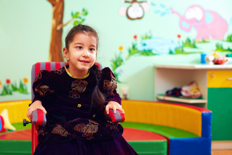 Smiling girl with neurodevelopmental disorder in a playroom sitting on a chair 