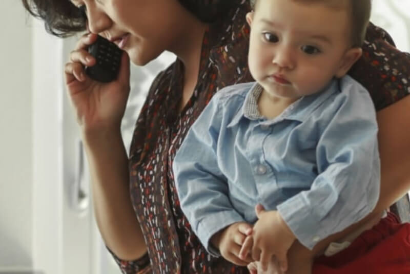 Young woman cradling phone in one hand, and holding infant with other arm.