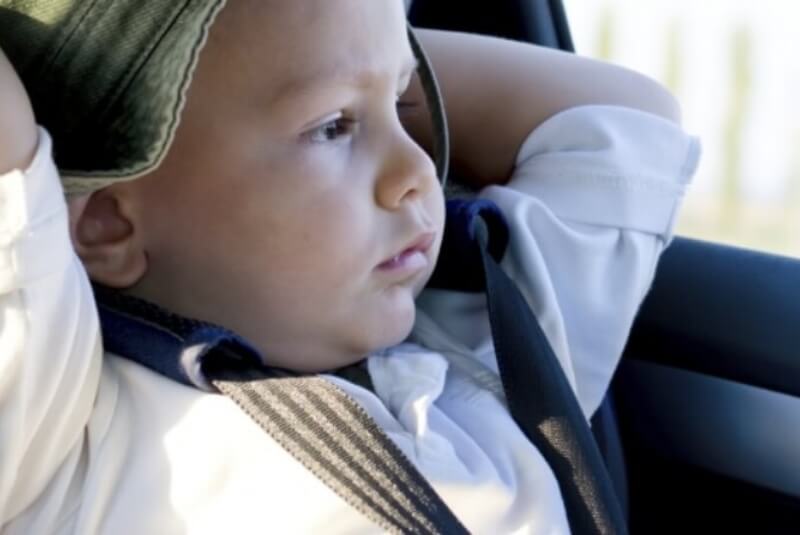 Young child strapped into car seat, looking out the car passenger window.