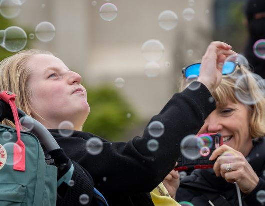 Girl in wheelchair smiles as carer blows bubbles