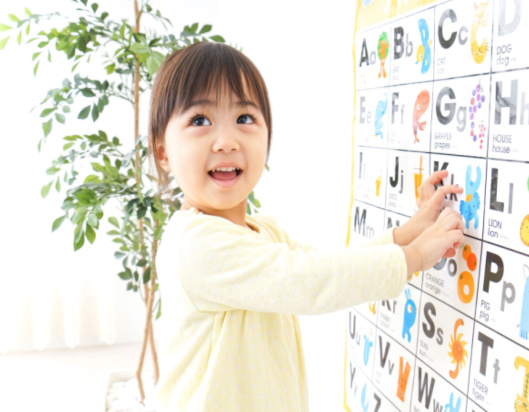 Little girl at school pointing to letters of the alphabet on a poster