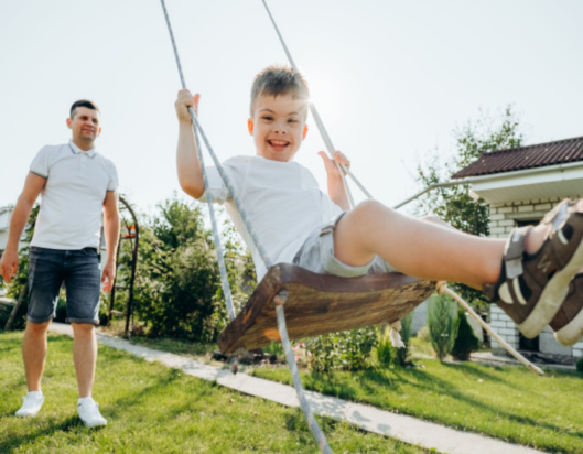 Dad pushes little boy on a swing in the sun