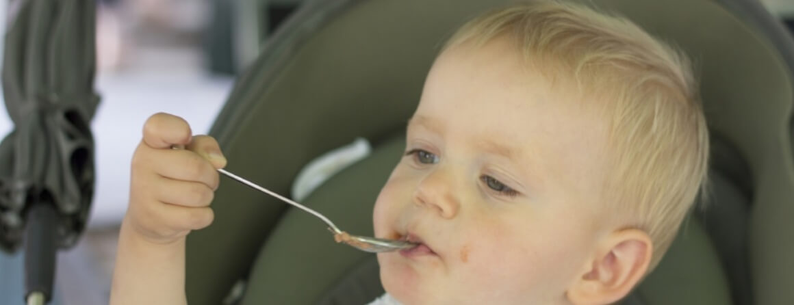 Young child holding a spoon and feeding themself.