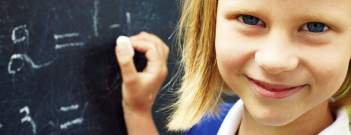 Smiling girl looking toward camera while writing on chalkboard.
