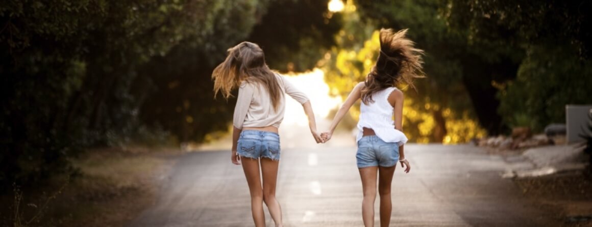 Two young girls walking in middle of the road, holding hands.