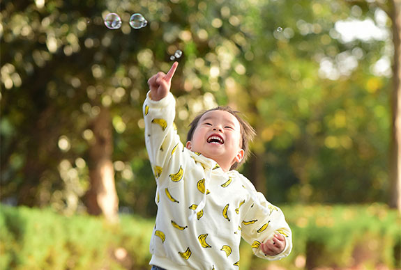 Child jumping to reach bubbles in the sky