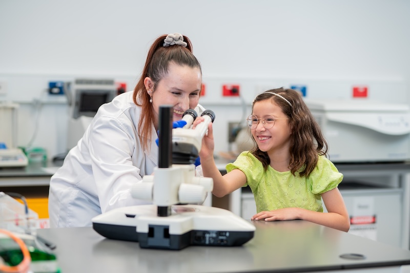 Child and researcher looking through microscope