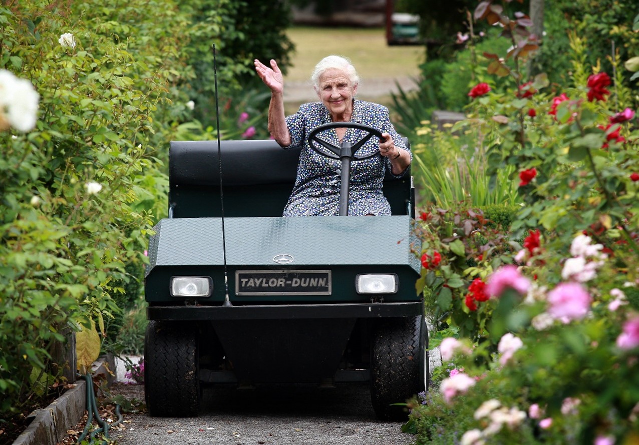 Dame Elisabeth Murdoch waving from a buggy in gardens