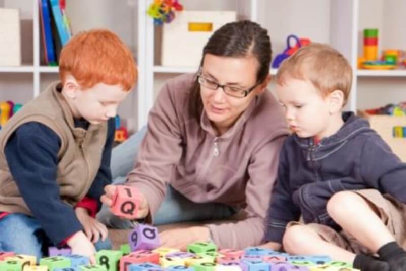 Woman with two boys working with letter and number blocks