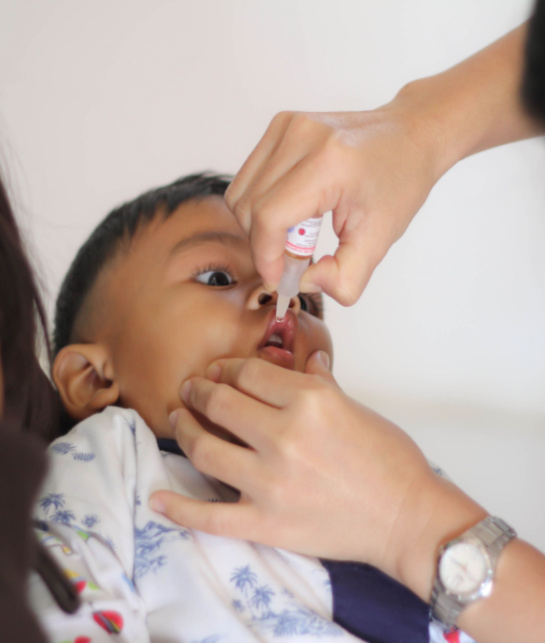 Little boy being held by mum while given oral vaccine
